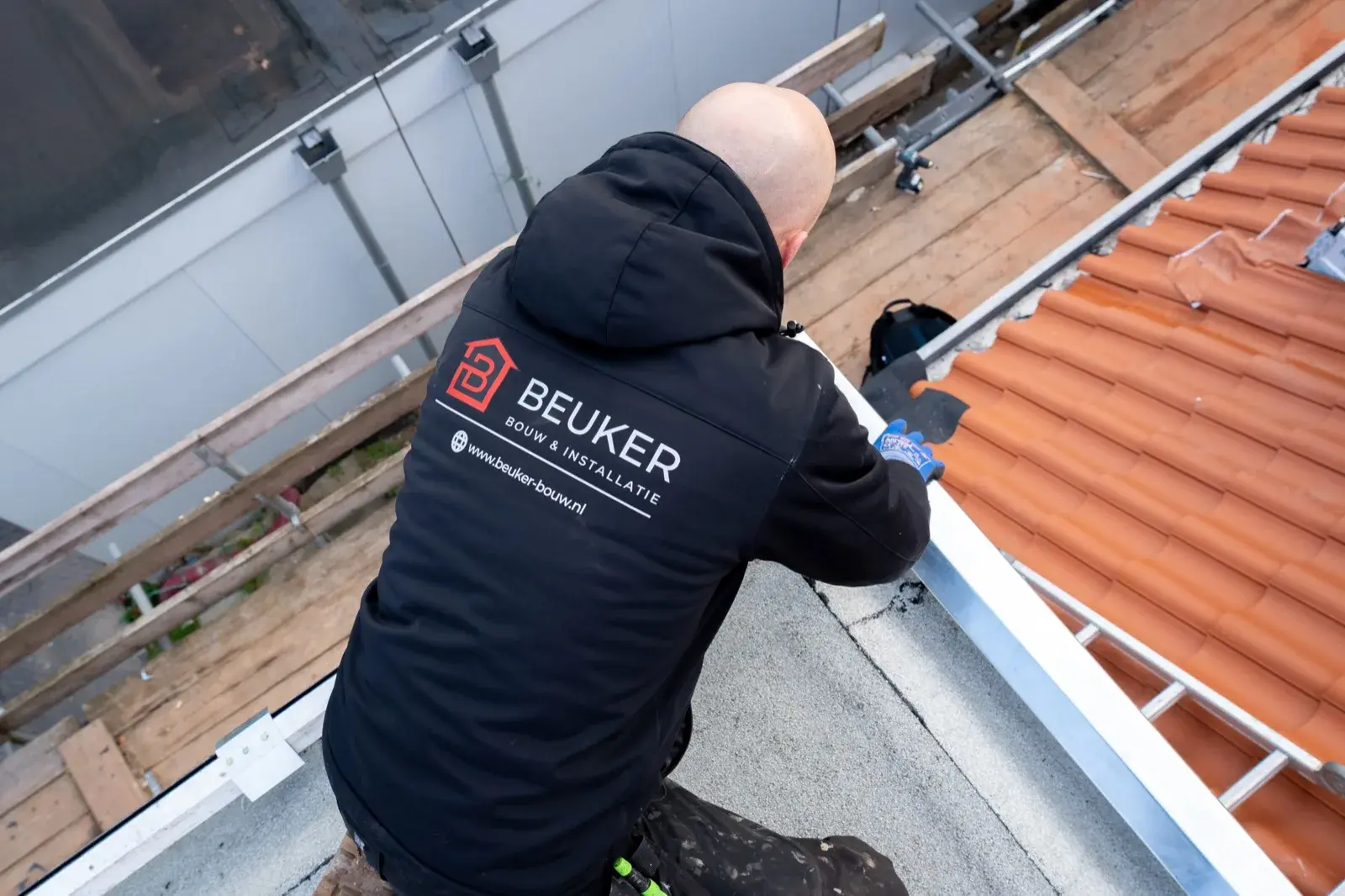 Dakdekker in bedrijfsjas van Beuker Bouw & Installatie werkt op een plat dak aan de metalen aansluiting met een pannendak